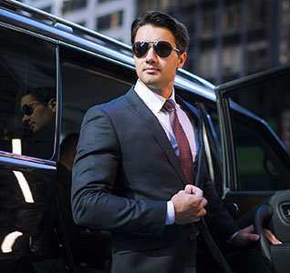 Handsome young businessman arriving in executive car wearing a suit and sunglasses in a city